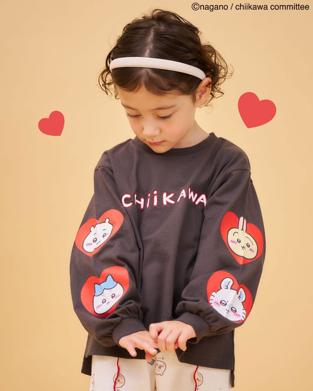 アニメちいかわ アソートTシャツ チャコールグレーを着た子ども。胸にCHIIKAWAのロゴ、両袖にハート型のパッチでキャラクターの顔が並ぶ