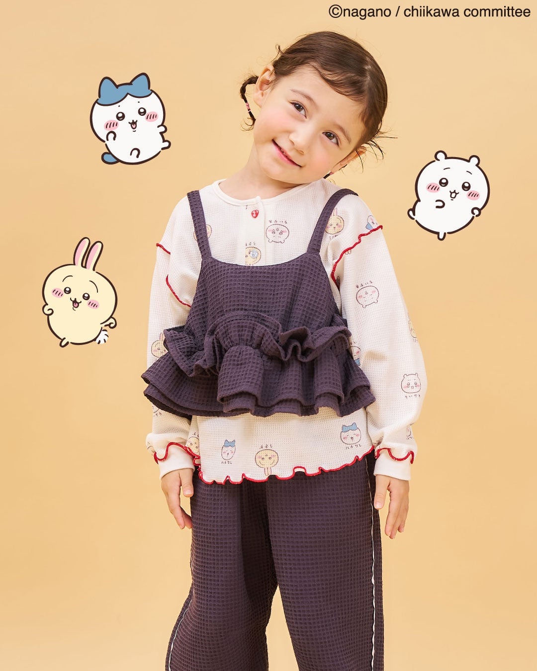 アニメちいかわ ワッフルヘンリーネックTシャツ アイボリーを着た子ども。ちいかわたちの顔の総柄に赤いメロウの縁取り