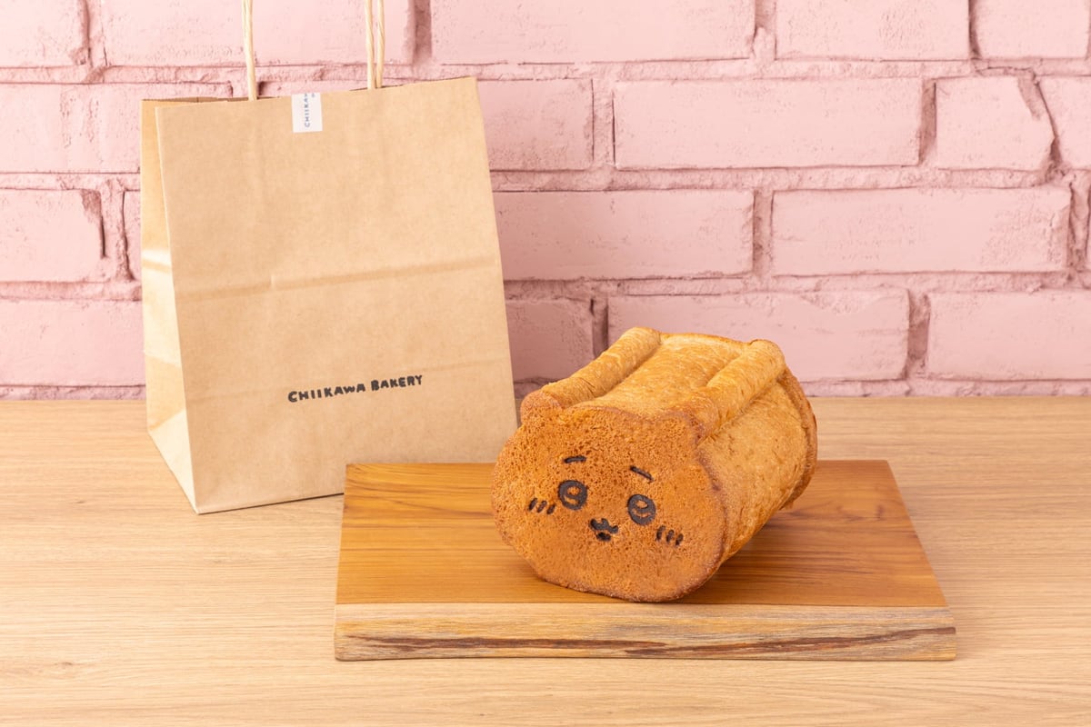沖縄限定「ちいかわ食パン(黒糖)」。ちいかわの顔の焼き印が入った食パンが木の板に載り、後ろにCHIIKAWA BAKERYの紙袋が置かれている