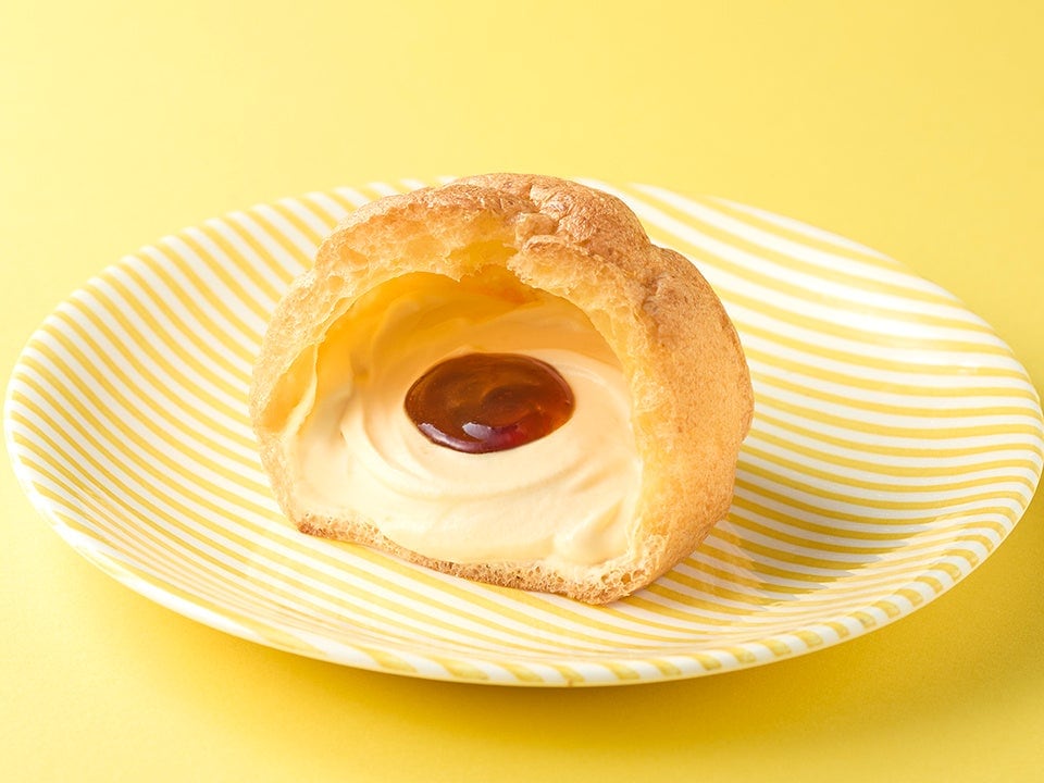 黄色いお皿にのった、カスタードクリームとカラメルが見えるシュークリームの断面