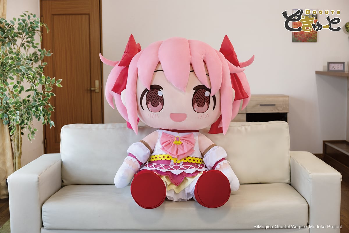 ソファに座った約100cmの「超特大ぬいぐるみ 鹿目まどか」。ピンクの髪に赤いリボン、白とピンクの魔法少女衣装、赤い靴