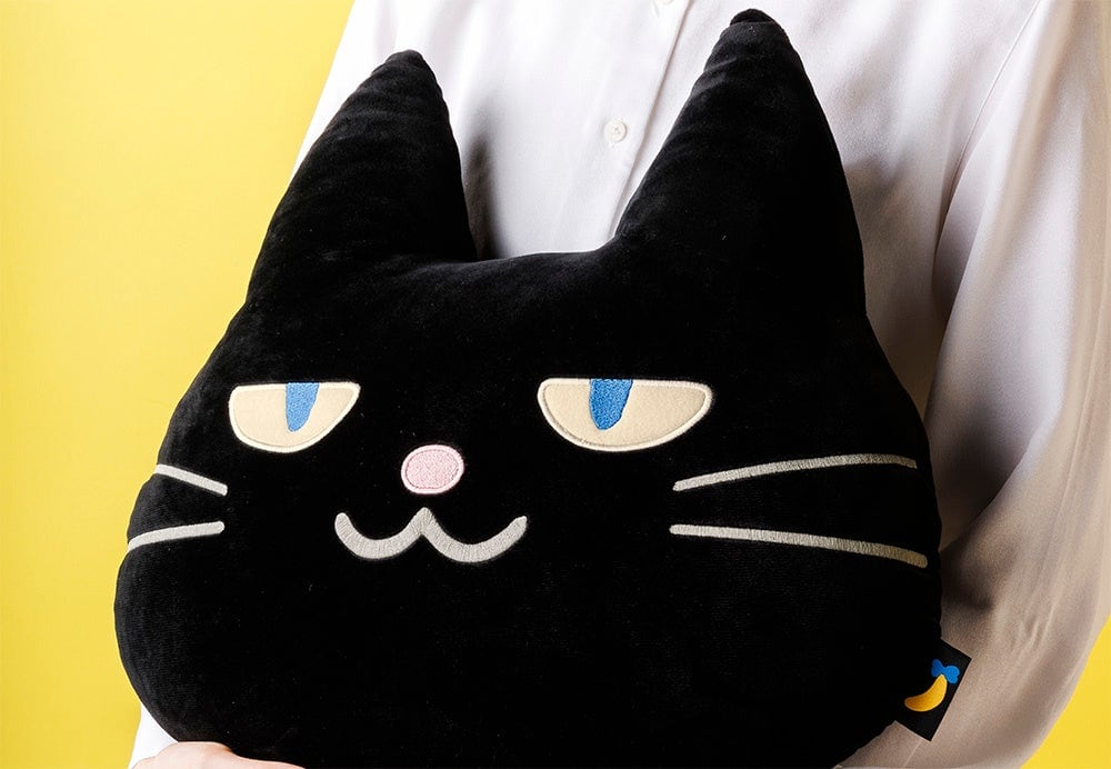 黒猫の顔をかたどったクッションを抱えた様子